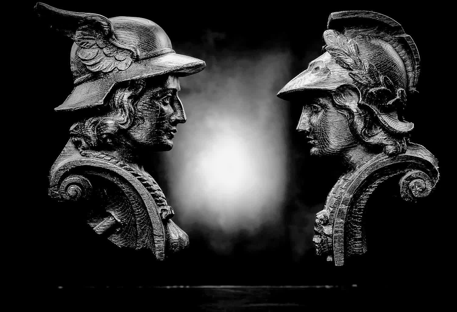 Two ancient bronze busts facing each other, a light in the gap between them.